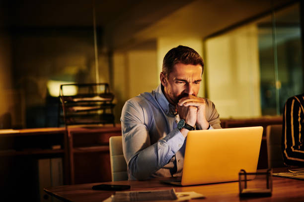 His nerves are shot Shot of a mature businessman looking anxious while working on a laptop in an office at night nail biting stock pictures, royalty-free photos & images