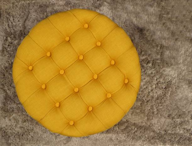 ボタンと正方形を持つ丸い生地黄色のプーフのトップビュー。グレーのカーペットの背景 - ottoman ストックフォトと画像