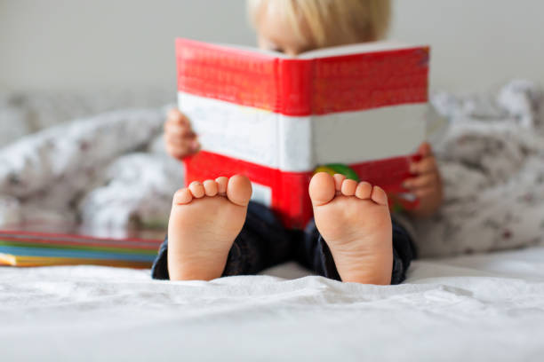 dulce niño pequeño, libro de lectura en casa, sentado en la cama, un montón de libros - child book reading baby fotografías e imágenes de stock
