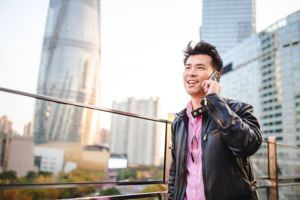 азиатский человек делает телефонный звонок на ходу - low angle view macho men urban scene стоковые фото и изображения