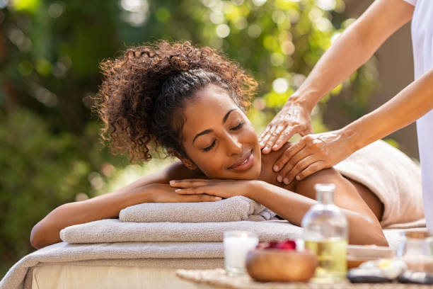 Beautiful woman relaxing with back massage Beautiful woman receiving back massage at resort spa. Happy african american girl receiving back massage outdoor. Relaxed girl lying on spa bed with eyes closed while getting a beauty treatment. spa lady stock pictures, royalty-free photos & images