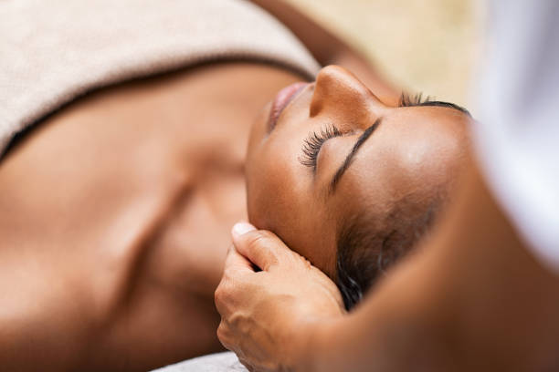 Black woman getting head massage Beautiful african woman getting face massage in beauty spa. Black girl with closed eyes relaxing in outdoor spa while getting head massage. Serene woman relaxing outdoor in a beauty center. spas and spa treatments stock pictures, royalty-free photos & images