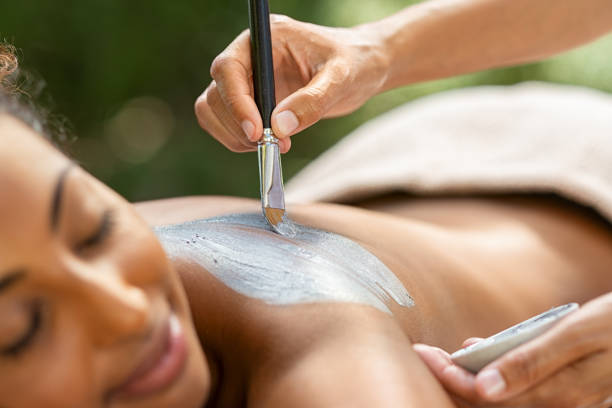 African woman receiving mud spa treatment Hands of masseuse applying mud mask on african woman back. Young african american girl relaxing with eyes closed while beautician applying exfoliation clay on shoulder. Woman at resort doing clay mask exfoliation. green clay stock pictures, royalty-free photos & images
