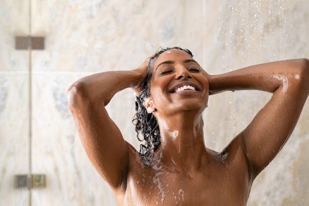 African woman washing hair under shower Young woman washing hair in shower at luxury spa. Woman washing her curly hair with shampoo and a lot of lather. Carefree black girl taking a long hot shower washing her hair in a modern bathroom.. body care shower stock pictures, royalty-free photos & images