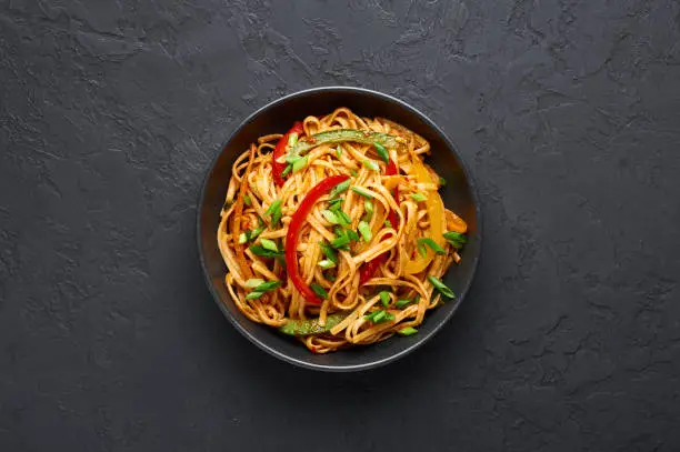 Vegetarian Schezwan Noodles or Vegetable Hakka Noodles or Chow Mein in black bowl at dark background. Schezwan Noodles is indo-chinese cuisine hot dish with udon noodles, vegetables and chilli sauce