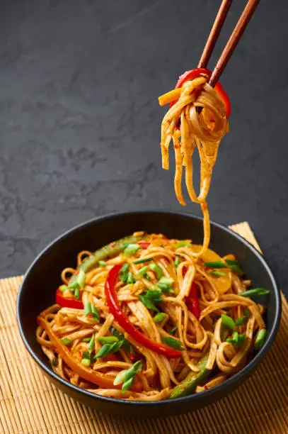 Vegetarian Schezwan Noodles or Vegetable Hakka Noodles or Chow Mein in black bowl at dark background. Schezwan Noodles is indo-chinese cuisine hot dish with udon noodles, vegetables and chilli sauce