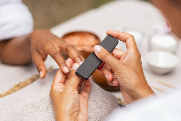 Woman using a buffer to file nail Close up of african hands of a qualified manicurist filing the nails of a young woman. Hands during manicure care session. Detail of a girl in a nail salon receiving manicure. fingernail stock pictures, royalty-free photos & images