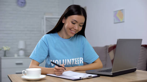 Female volunteer working laptop and writing notes sitting table, charity project