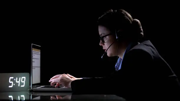 Female call-center employee in formal suit and headphones working at night shift