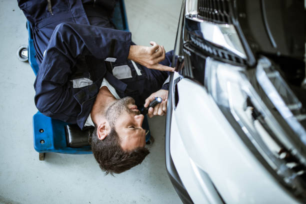 Above view of auto mechanic analyzing car problems with a lamp in a workshop. High angle view of young car mechanic analyzing a car with a lamp. car mechanic top view stock pictures, royalty-free photos & images