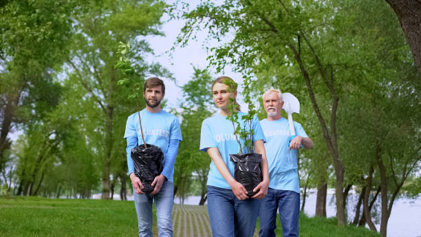 istock Responsible eco activists walking park path holding green tree saplings shovel 1176496423