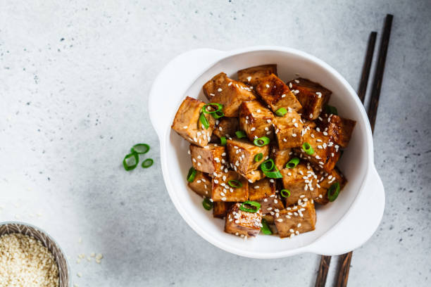 Fried tofu in teriyaki sauce in white bowl, top view. Vegan food concept. Fried tofu in teriyaki sauce in a white bowl. Vegan food concept. tofu stock pictures, royalty-free photos & images