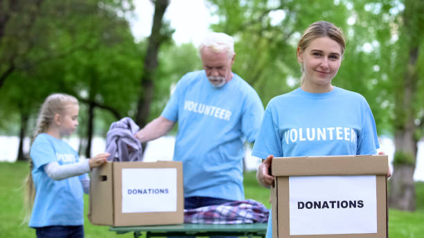 istock Pretty female volunteer holding box, activists sorting clothes on background 1176496687