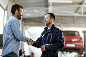 Happy car mechanic shaking hands with his customer in auto repair shop.