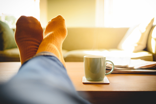 Relaxing at the weekend with a hot cup of tea of coffee and the newspapers. Man wearing orange socks has his legs crossed, feet up on the coffee table.