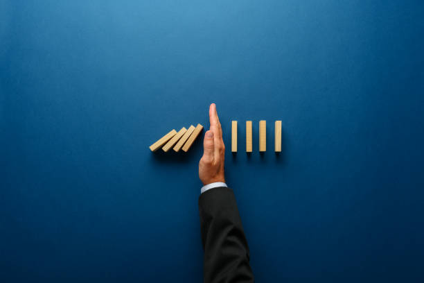 Business crisis management conceptual image Top view  of businessman hand stopping falling dominos in a business crisis management conceptual image. domino effect stock pictures, royalty-free photos & images