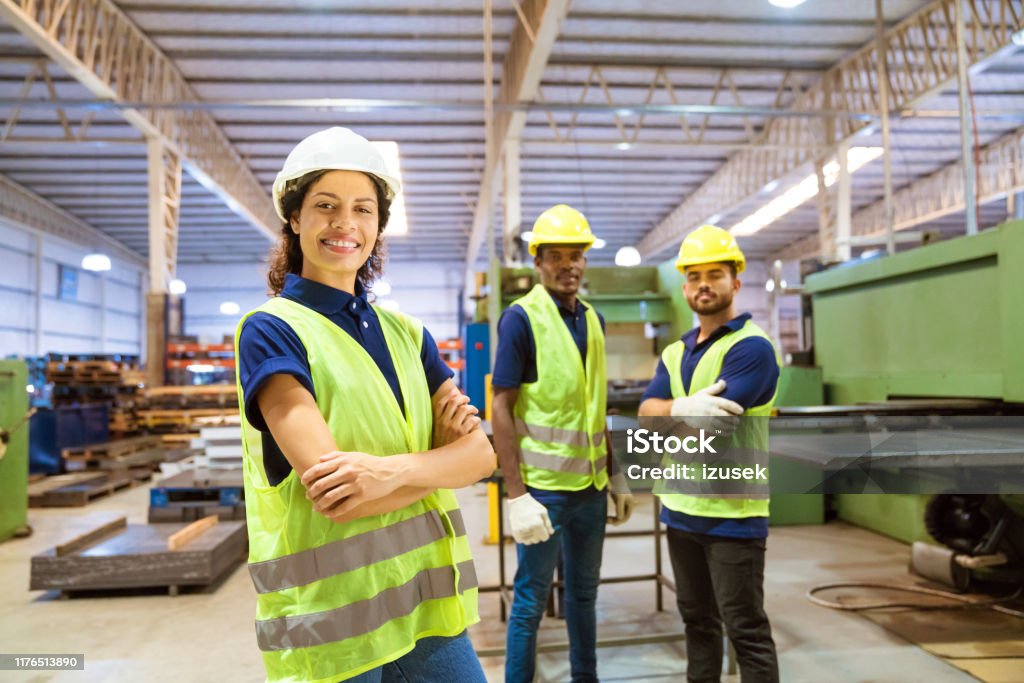 Smiling female engineer against male colleagues Portrait of smiling female engineer standing against colleagues. Expertise are working in industry. They are into manufacturing occupation. Engineer Stock Photo