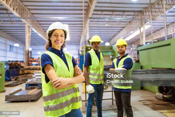 Smiling Female Engineer Against Male Colleagues Stock Photo - Download Image Now - Engineer, Factory, Hardhat
