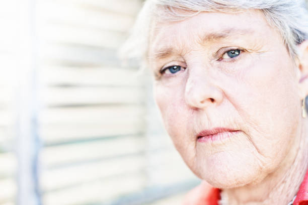 istock Serious senior woman standing by sunlit blinds 1176518770