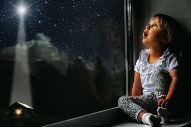 the child looks out the window into the night sky stock photo