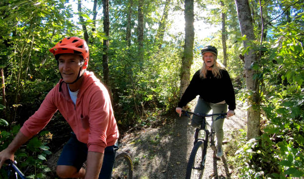 pareja de bicicleta de montaña a través del bosque al amanecer - beautiful red pink wood fotografías e imágenes de stock