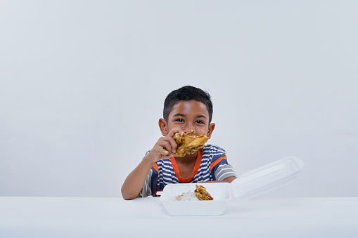 Schoolboy eating fried chicken fastfood on white background