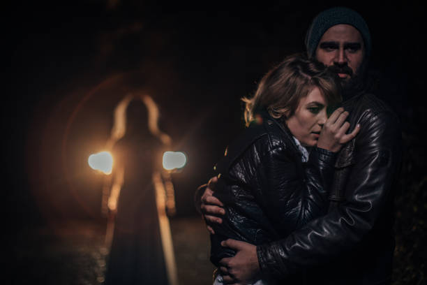 Man and woman are scared and hugging, witch is standing behind them, halloween night.