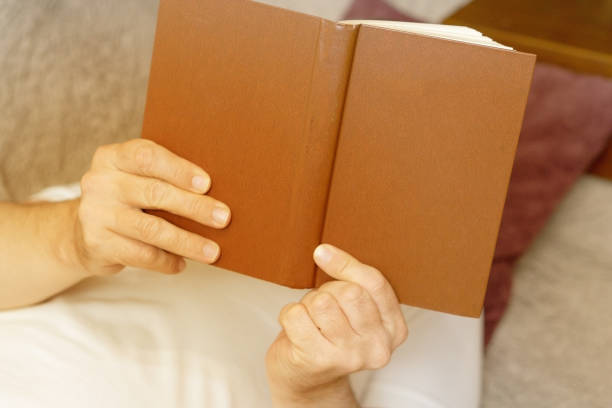 istock A man is reading a brown cover book while lying on a sofa. Close-up 1176534891