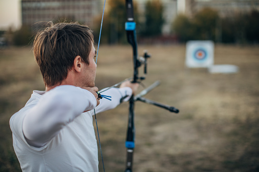 One man, young archer with bow and arrow training alone outdoors.