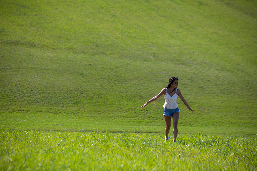 Beautiful young happy girl walking on a green field outside on a sunny day