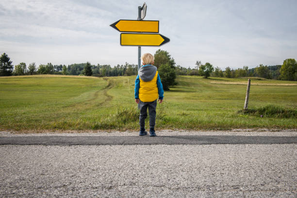 Left or Right, Little boy looking for direction in a beautiful green plateau Little boy looking for road direction on a beautiful green plateau. Slovenia, Europe. crossroads sign stock pictures, royalty-free photos & images