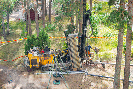 Espoo, FINLAND - JULY 3, 2019:Geothermal heat pump installation in Eco friendly apartment house. Drilling rig in yard. Worker in hard hat drilling a borehole for geothermal heating system.