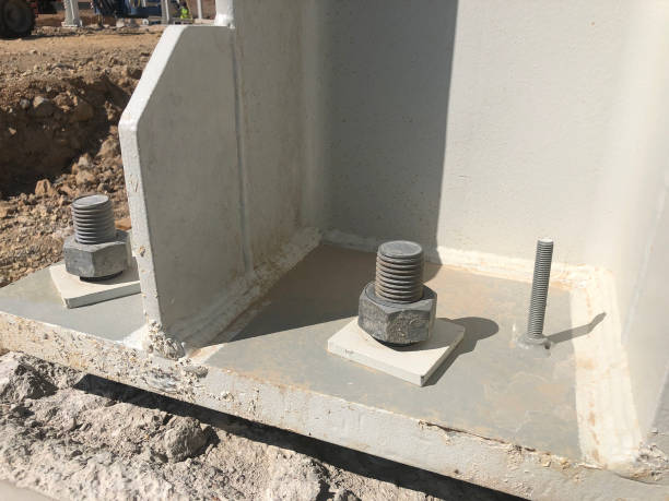Metal pillar fastened to basement with anchor bolts and nuts. Supporting structures, metal frame of prefabricared building.
