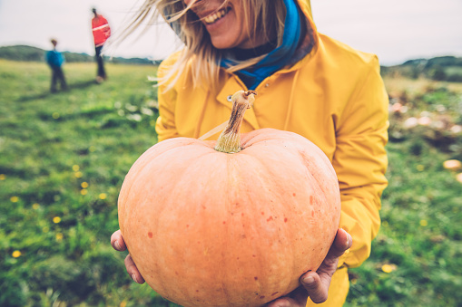 Happy Young Woman holding an Orange Pumpkin in hands