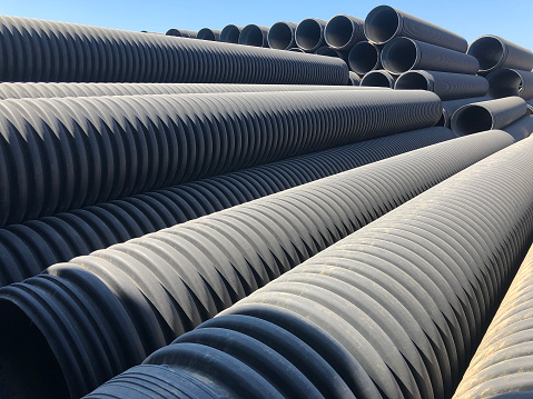 Stacked corrugated pvc-pipes at the outdoor warehouse. Drainage, plumbing, stormwater equipment.