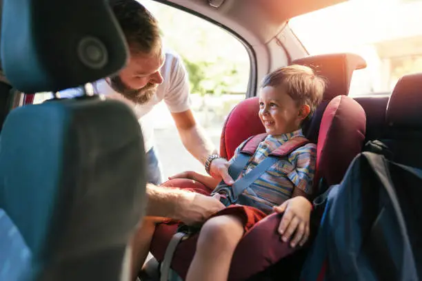 Single father getting his son buckled up with safety belts before starting their trip