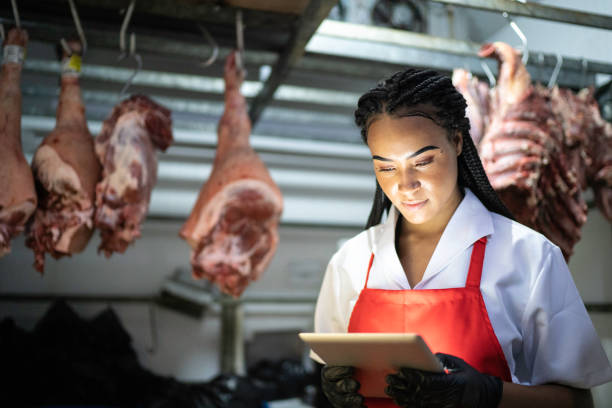 Female butcher using digital tablet to analyze products in a meat locker Female butcher using digital tablet to analyze products in a meat locker meat locker photos stock pictures, royalty-free photos & images