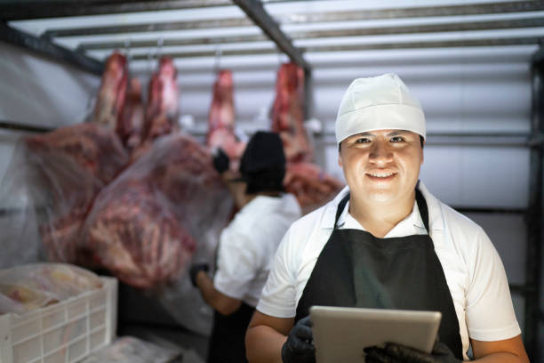 Portrait of a butcher using digital tablet to analyze products in a meat locker Portrait of a butcher using digital tablet to analyze products in a meat locker meat locker photos stock pictures, royalty-free photos & images