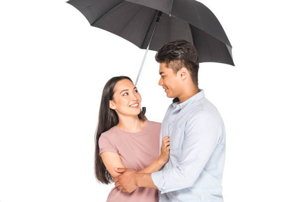 istock happy asian couple hugging and looking at each other while standing under umbrella isolated on white 1176565381