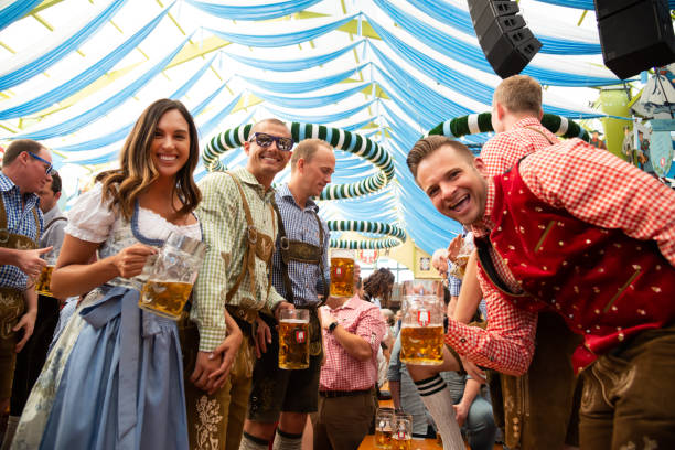 Beer Tent, Octoberfest in Munich, Germany Munich, Germany - September 21, 2019: Oktoberfest in Munich, Germany. A group of young people in beer hall, celebrating Oktoberfest on Theresienwiese. People are dressed in traditional clothes and holding beer glass. The Oktoberfest is the largest fair in the world and is held annually in Munich. alcoholism alcohol addiction drunk stock pictures, royalty-free photos & images