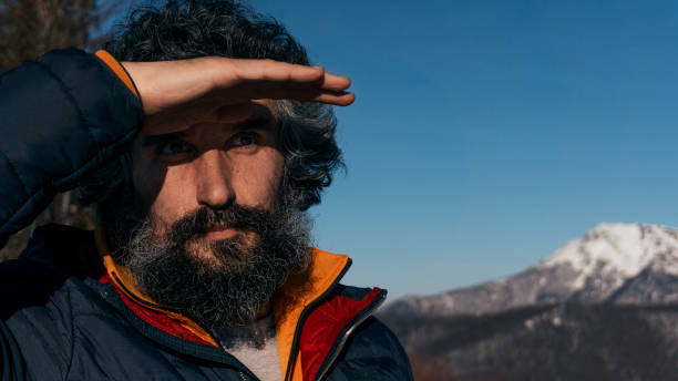 An Active Mature man in the Mountains, Taking Pictures with a Modern Camera, at the evening Sunlight. Back Lit, Alpine style, a Mountain Climbing Hike. A Backpacker at Bright Sunset over Clear Blue Sky. Photographing, Enjoying the Winter Mountain.