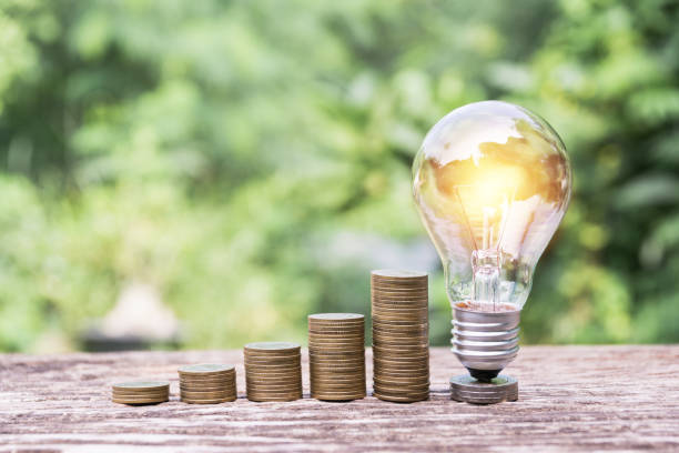 energiesparende glühbirne stapel von münzen auf naturhintergrund. - saving electricity stock-fotos und bilder