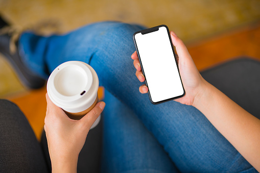 Woman holding a blank white screen smart phone and sitting on a couch.