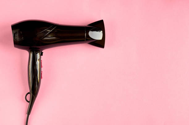 Black hair dryer on pink background composition.