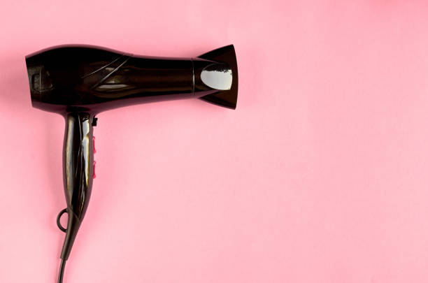Black hair dryer on pink background composition. stock photo