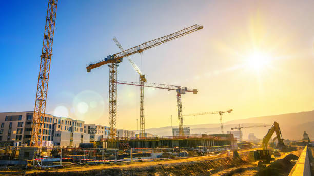 large construction site including several cranes, with clear sky and the sun - industrial equipment trackhoe construction site construction vehicle imagens e fotografias de stock