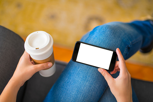 Woman sitting on a couch and holding a blank screen smart phone.