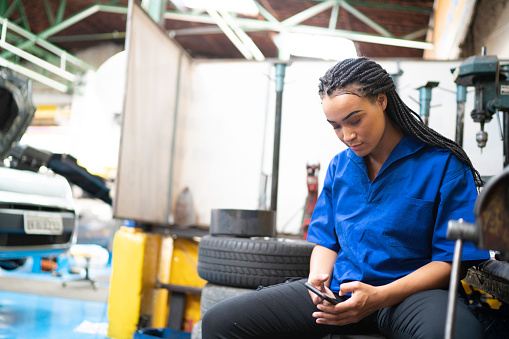 Female mechanic relaxing using mobile at break in a auto repair shop