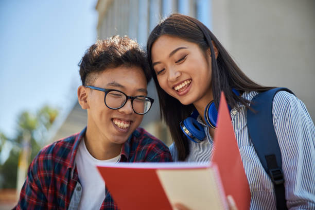 istock Smiling Asian students are looking at notebook outdoors 1176588021