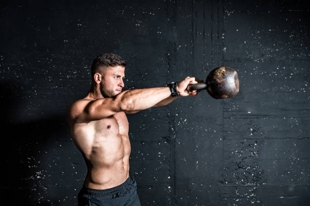 junge starke schwitzende fokussiert eisfit muskel mann mit großen muskeln halten schwere kesselglocke für swing cross training harten kern training in der turnhalle - crossfit kettle bell equipment weights stock-fotos und bilder